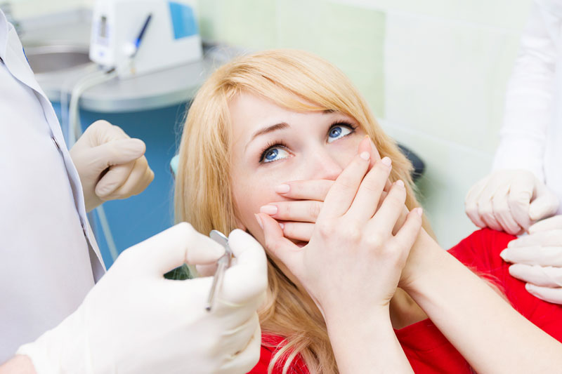 Woman fearful of dentist, hands over mouth