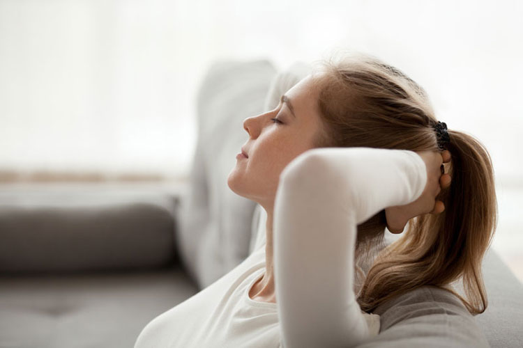 Woman sitting on couch hands behind head relaxing